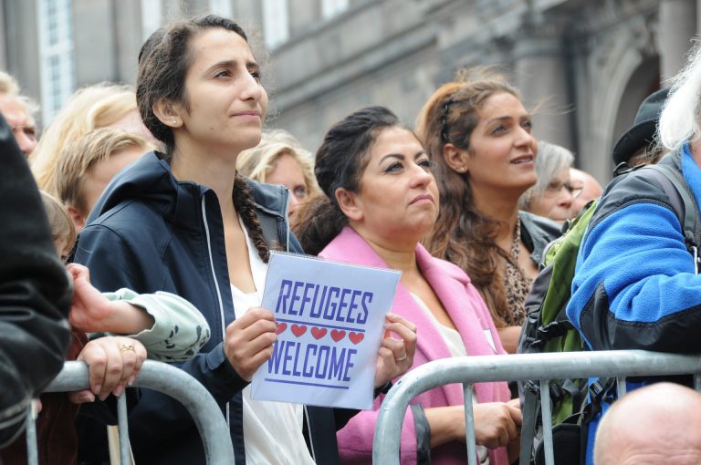 A woman holds a sign that reads refugees welcome at a peaceful rally
